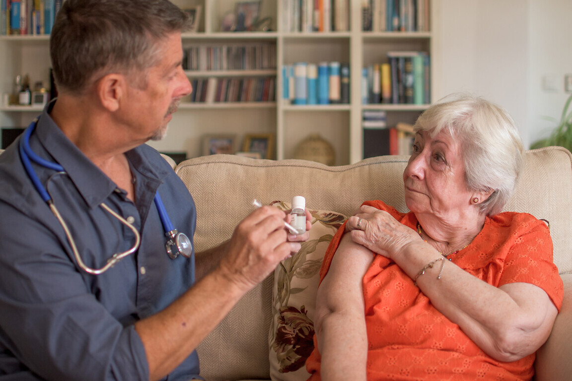 A doctor injects the winter flu jab into a elderly lady.