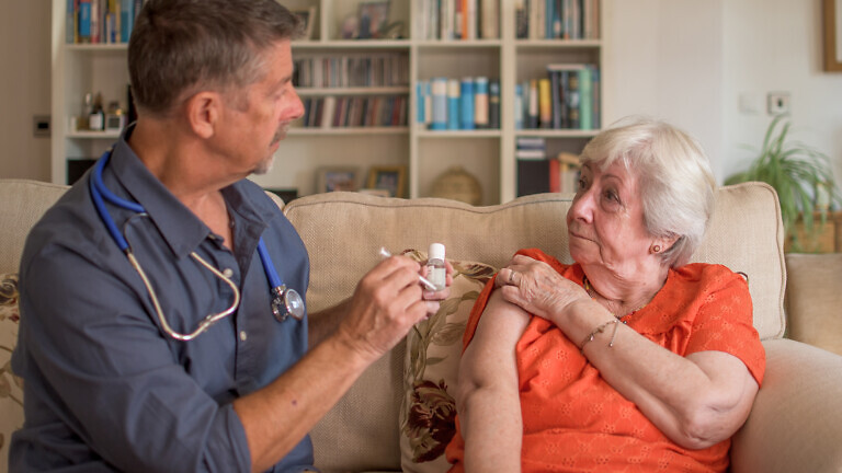 A doctor injects the winter flu jab into a elderly lady.