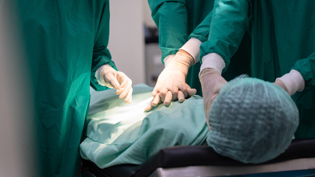 Close-up of Asian surgical team in green scrubs performing chest compressions on patient male in operating room. emergency teamwork efficiency healthcare in sterile room, heart failure case accident