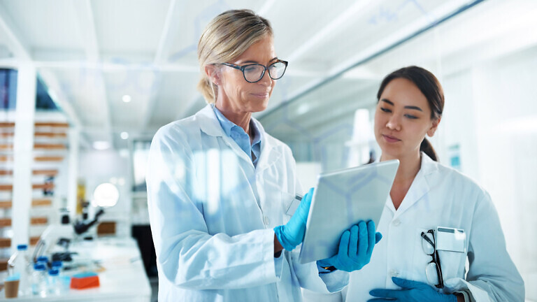 Women, scientist and discussion with tablet by glass, reading and review with results at pharma company. People, mentor and feedback with notes, application and medical research for mpox vaccine