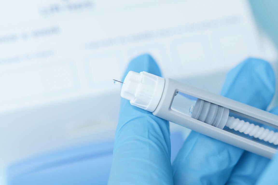 Close up on a needle on diabetic medication pen. Hands with blue glowes taping pen. High quality photo