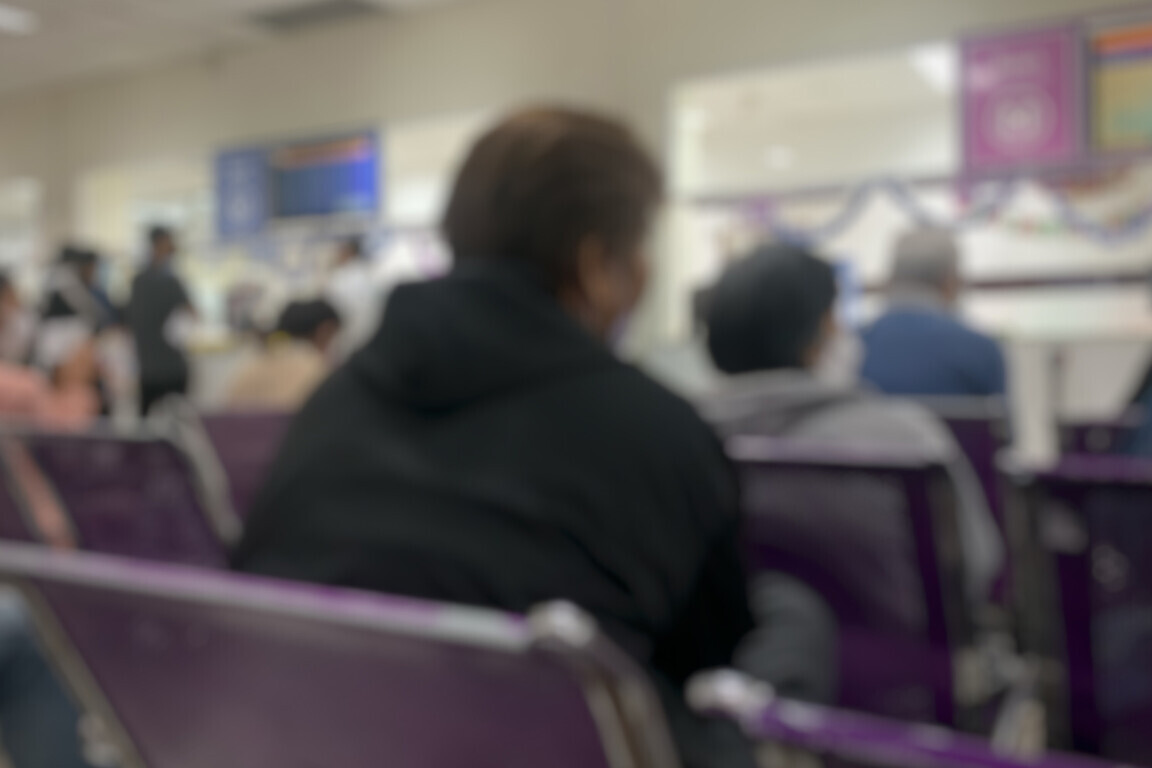 Blurred image of a large number of patients sitting in a large hospital waiting room.