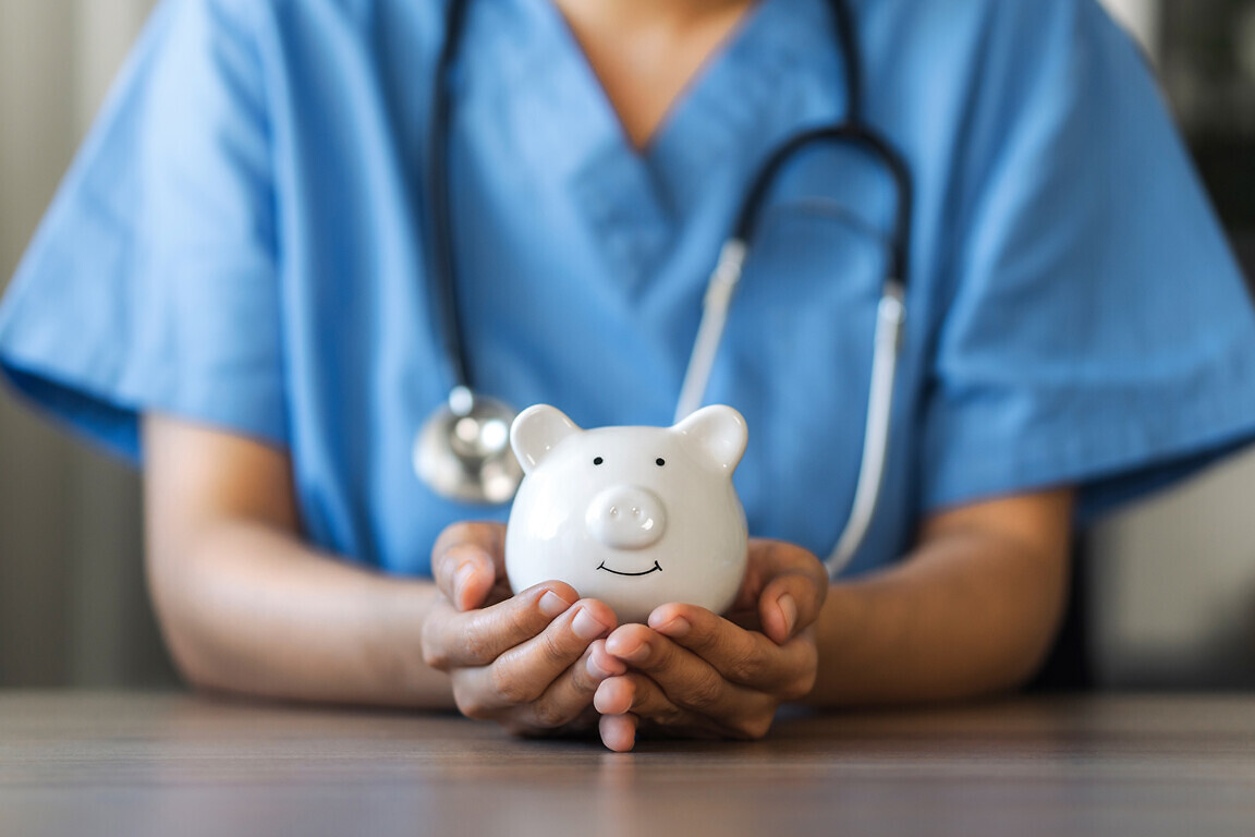 Nurse or doctor with stethoscope holding piggy bank in hand.