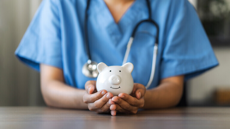 Nurse or doctor with stethoscope holding piggy bank in hand.
