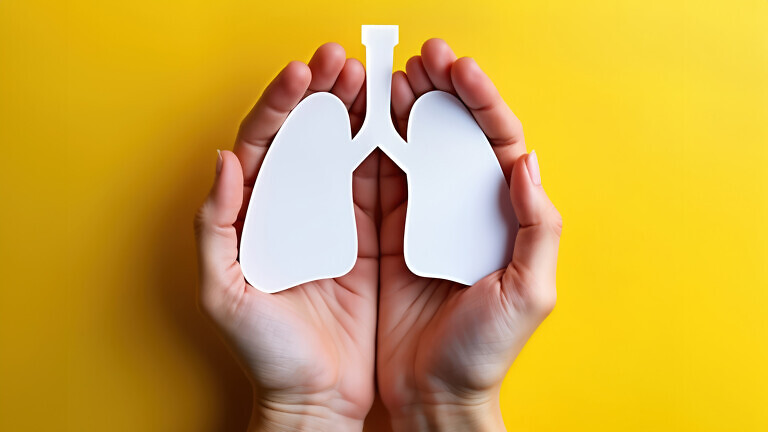 Adult hands hold paper lungs against yellow background.