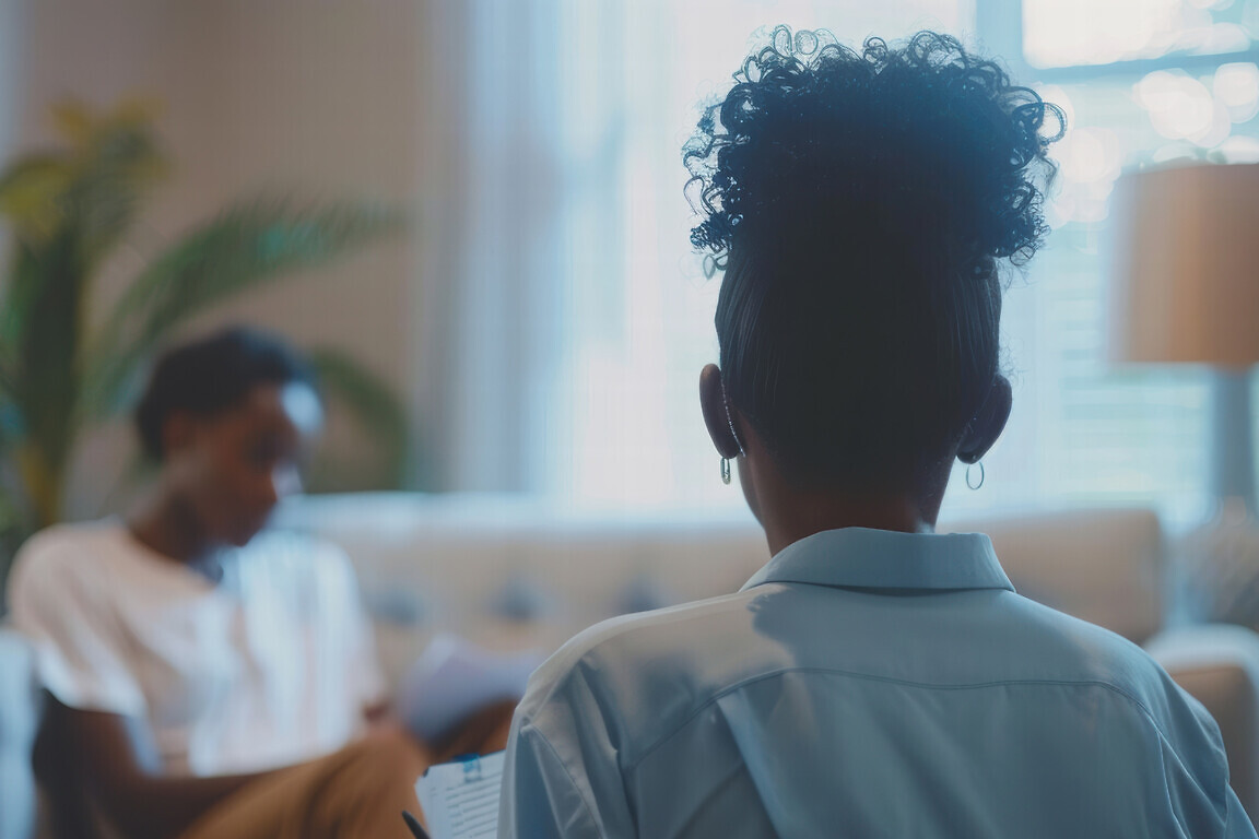 A woman therapist sitting on a couch taking notes with a patient.