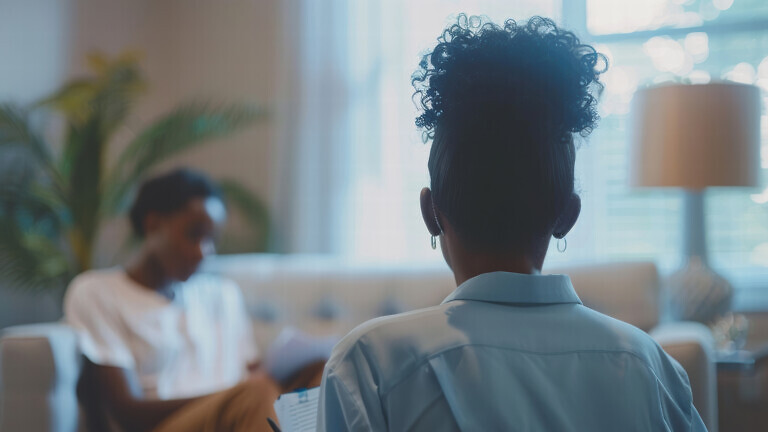 A woman therapist sitting on a couch taking notes with a patient.