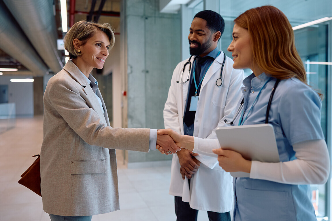 Smiling medical sales representative greeting healthcare workers at clinic.