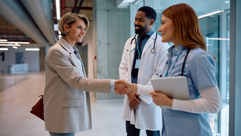 Smiling medical sales representative greeting healthcare workers at clinic.