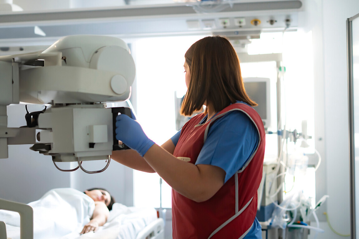 Radiologist positioning x-ray machine over patient lying in hospital