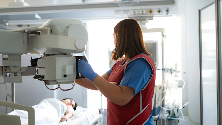 Radiologist positioning x-ray machine over patient lying in hospital