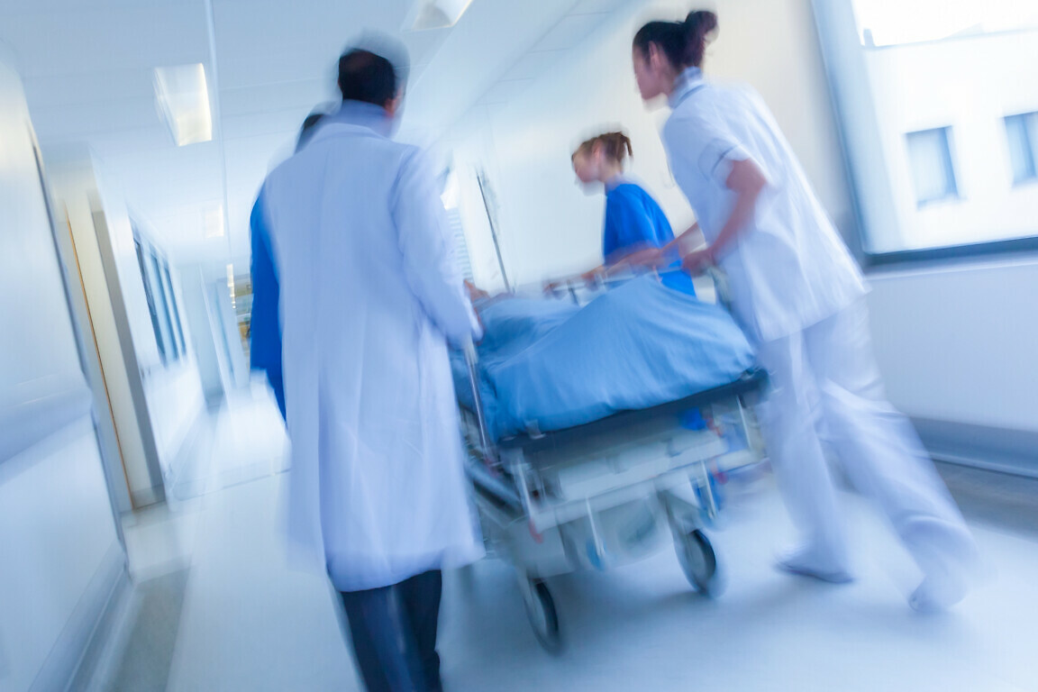 A motion blurred photograph of a patient on stretcher or gurney being pushed at speed through a hospital corridor by doctors & nurses to an emergency room