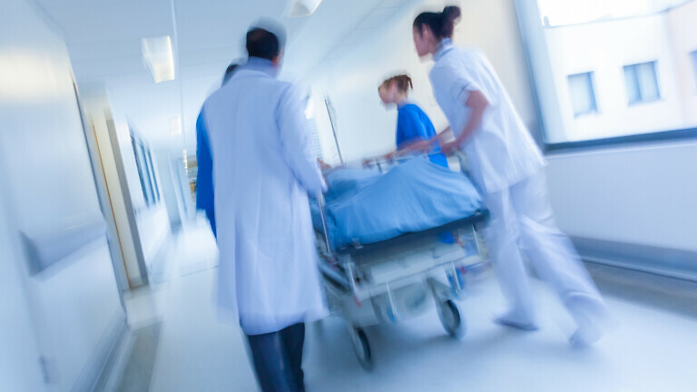 A motion blurred photograph of a patient on stretcher or gurney being pushed at speed through a hospital corridor by doctors & nurses to an emergency room