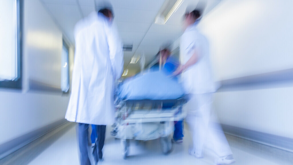 A motion blurred photograph of a patient on stretcher or gurney being pushed at speed through a hospital corridor by doctors & nurses to an emergency room