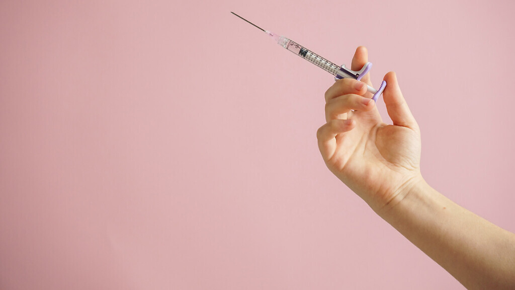 gloved hand holding multiple colorful syringes