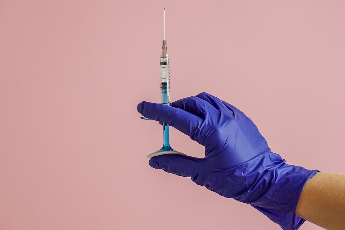 gloved hand holding multiple colorful syringes