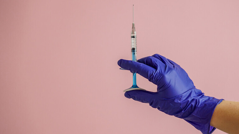 gloved hand holding multiple colorful syringes