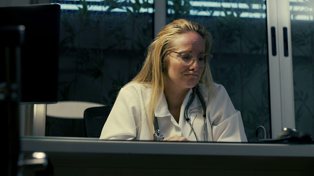 Female doctor in distress during night shift, facing intense emotional pressure while sitting at desk in clinical setting, struggling with overwhelming workload