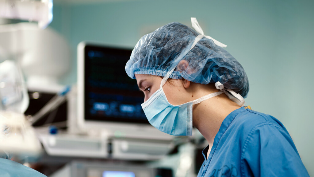 Surgeon in blue scrubs and surgical mask.