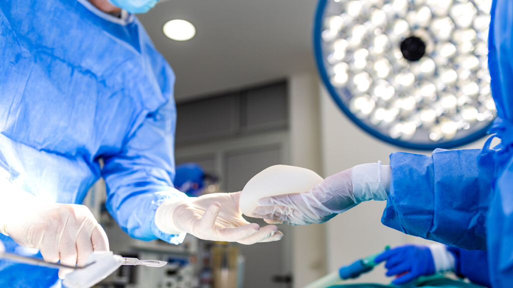Close up of surgeon hands passing silicone breast implant during plastic surgery.
