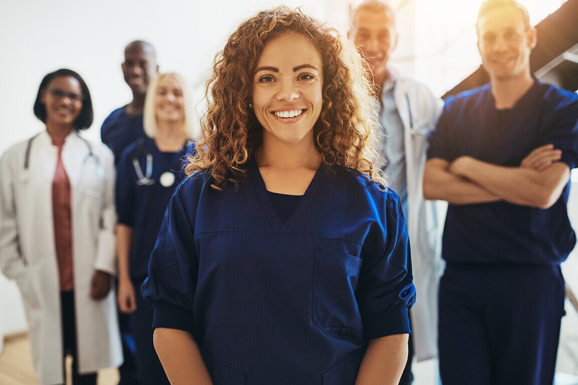 Smiling young female doctor standing in a hospital corridor with a diverse group of medical staff standing behind her