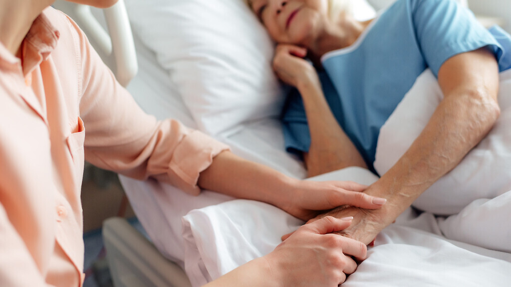 cropped view of daughter sitting near senior mother in bed and holding hands in hospital