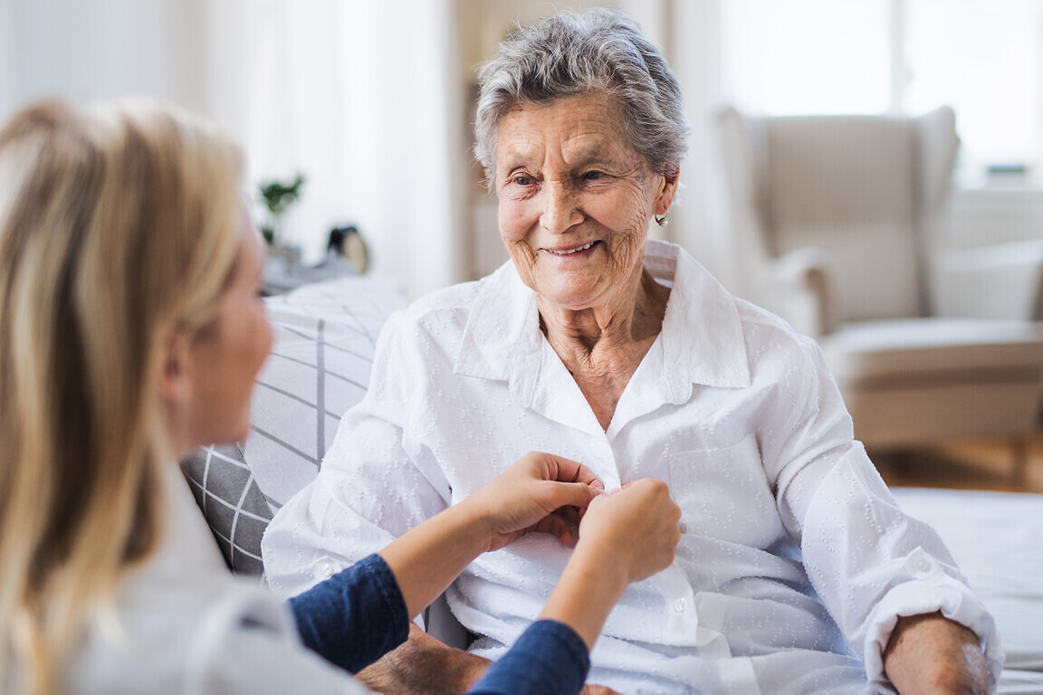 A health visitor helping a sick senior woman sitting on bed at home.