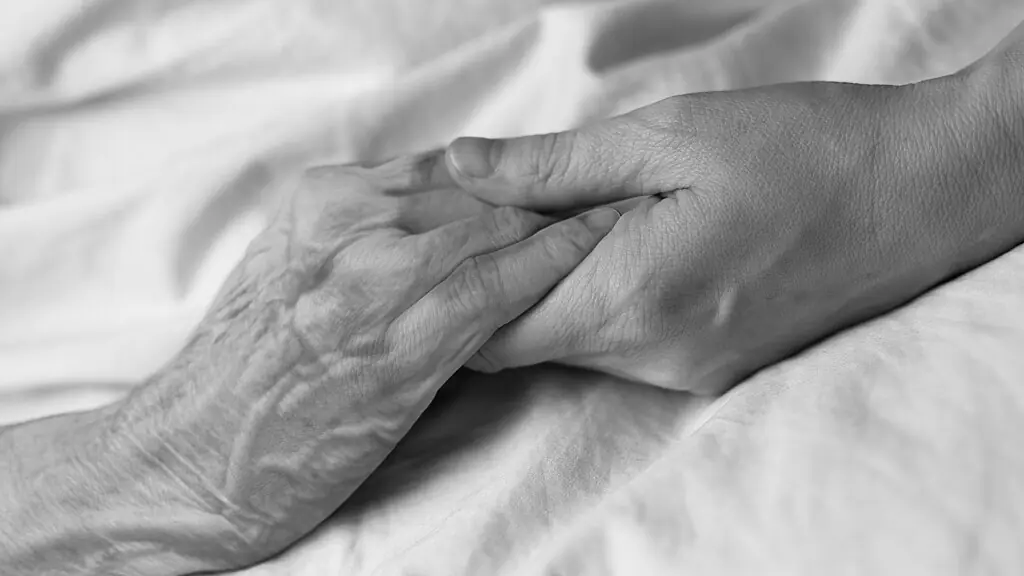 A young woman holding the hand of an old woman in a hospital bed.
