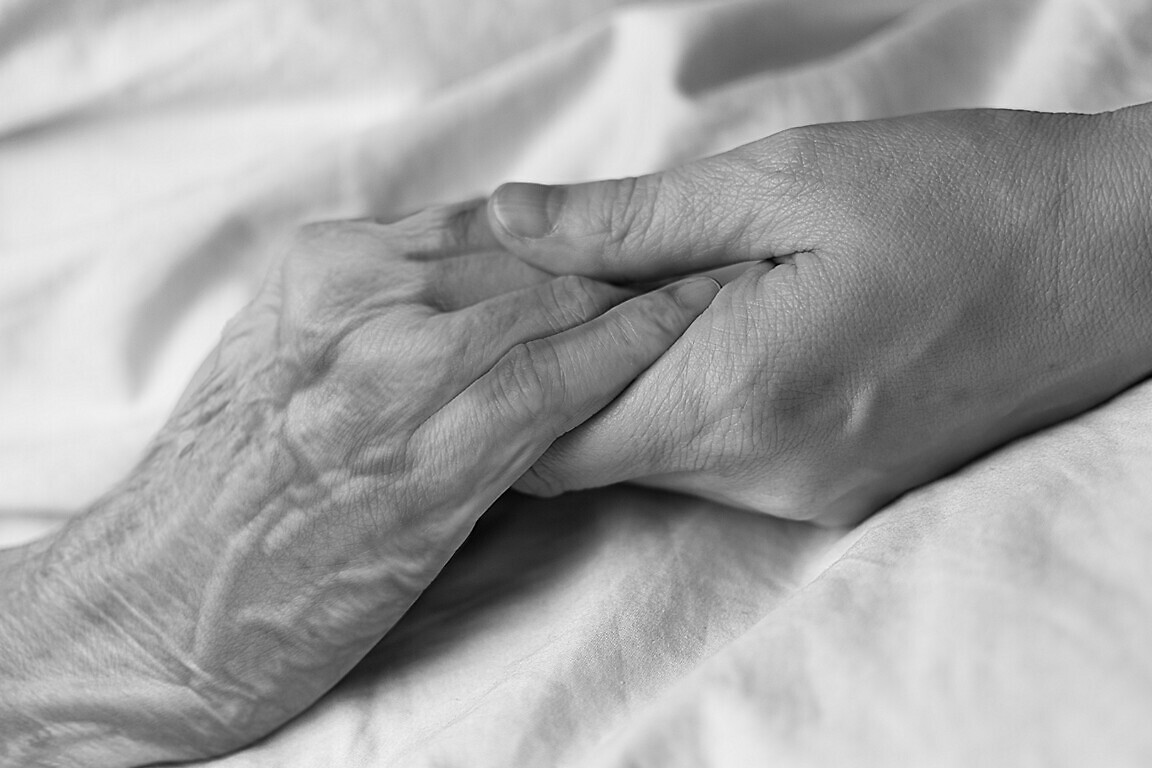 A young woman holding the hand of an old woman in a hospital bed.