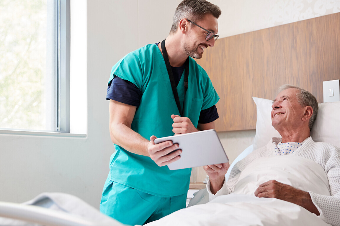 Surgeon Visiting And Talking With Senior Male Patient In Hospital Bed In Geriatric Unit