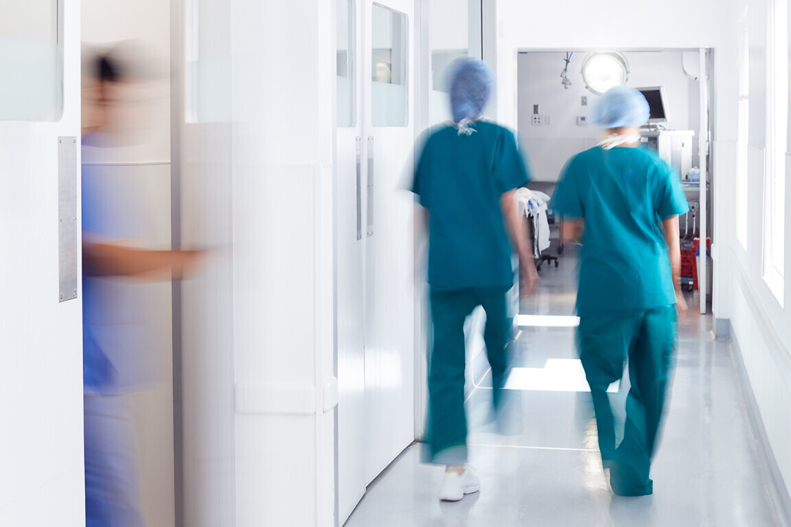 Motion Blur Shot Of Medical Staff Wearing Scrubs In Busy Hospital Corridor