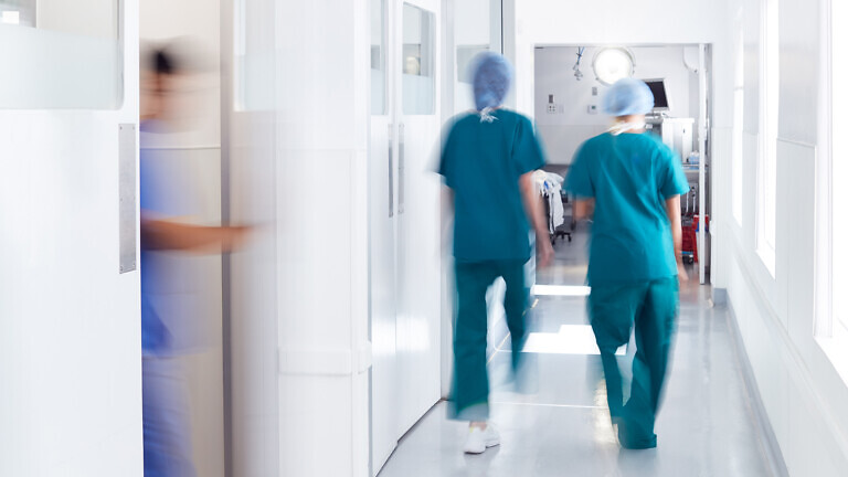 Motion Blur Shot Of Medical Staff Wearing Scrubs In Busy Hospital Corridor