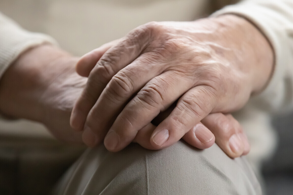 Close up of older male palms joined on his lap