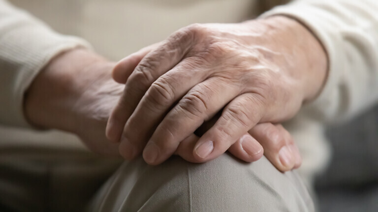 Close up of older male palms joined on his lap