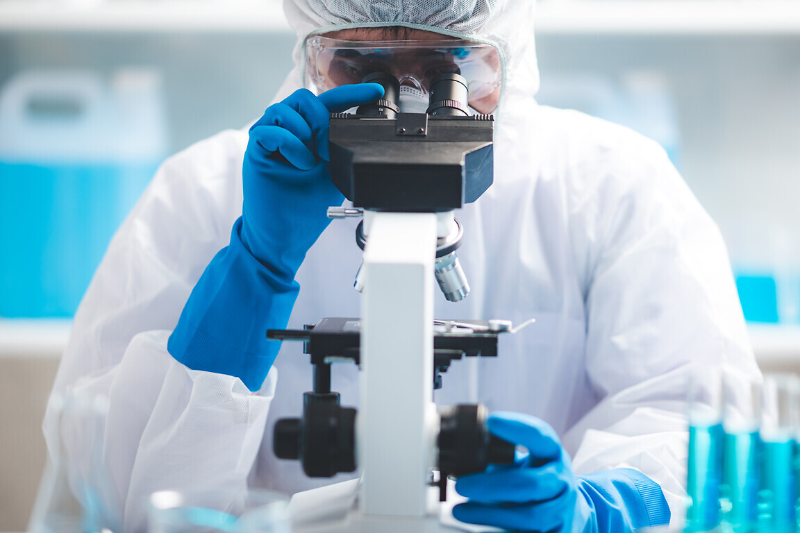 Scientist analyzing microscope slide at laboratory. Young woman technician is examining a histological sample, a biopsy in the laboratory of cancer research