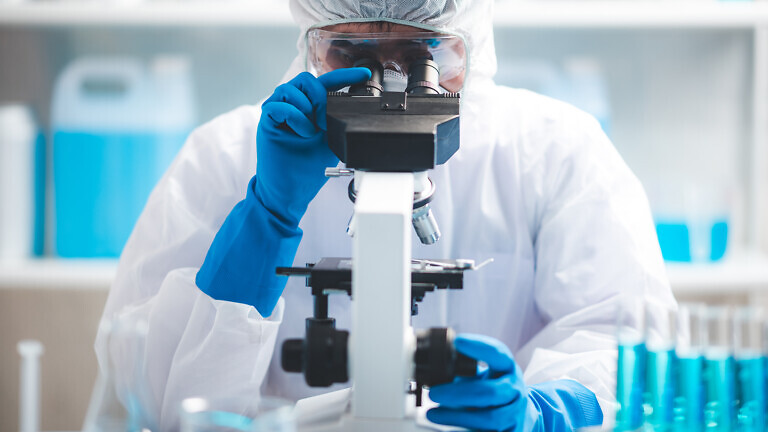 Scientist analyzing microscope slide at laboratory. Young woman technician is examining a histological sample, a biopsy in the laboratory of cancer research