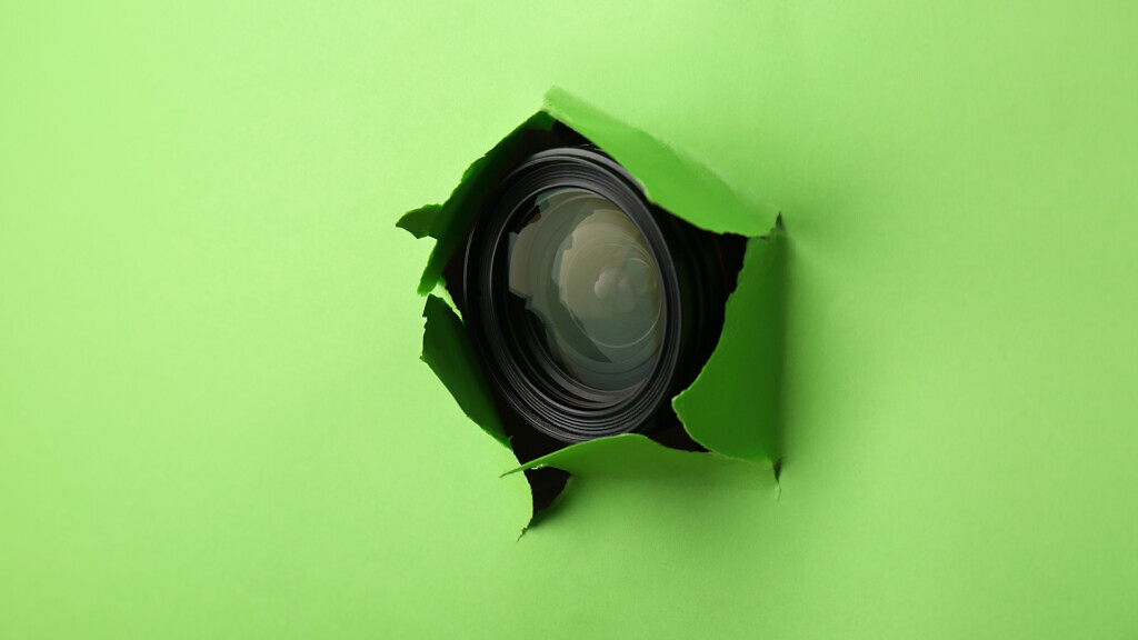 Hidden camera lens through torn hole in green paper