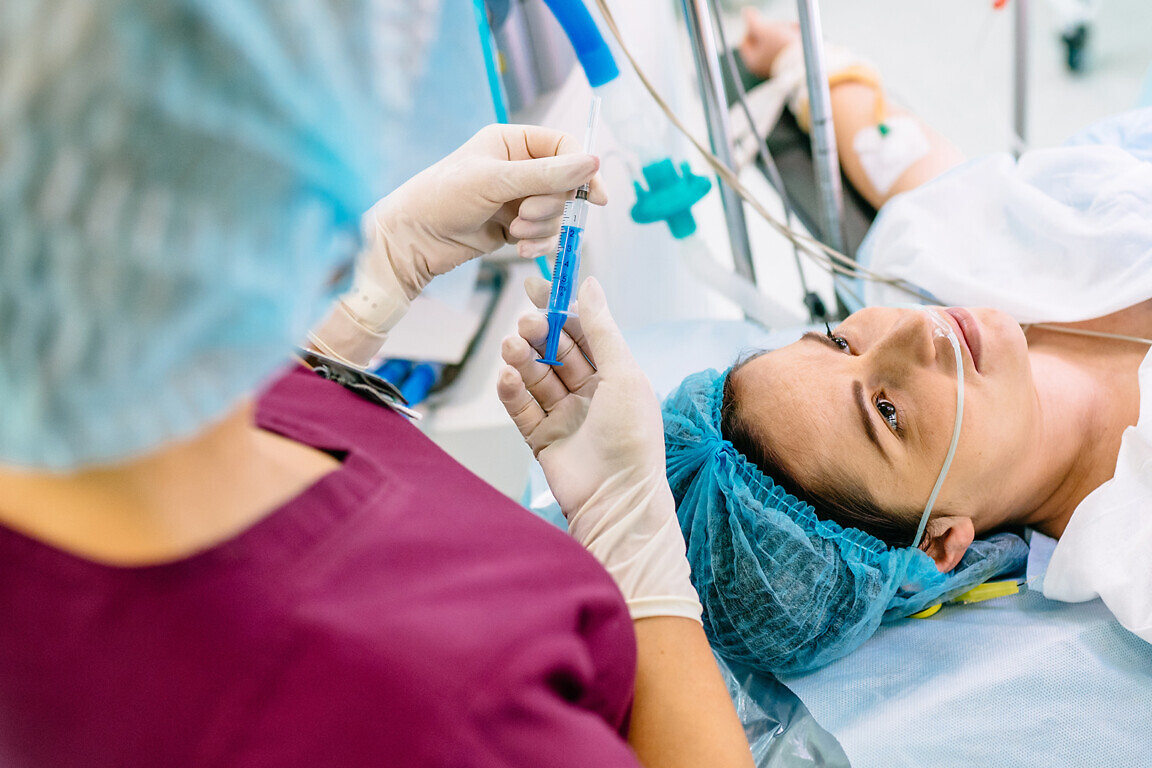 Anesthesia is administered through a syringe. Medical background. Medical doctor giving patient anesthesia before surgical operation inside modern hospital.