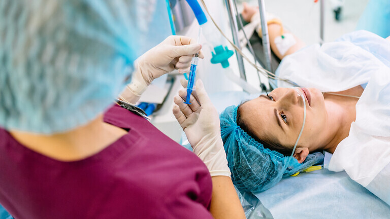 Anesthesia is administered through a syringe. Medical background. Medical doctor giving patient anesthesia before surgical operation inside modern hospital.