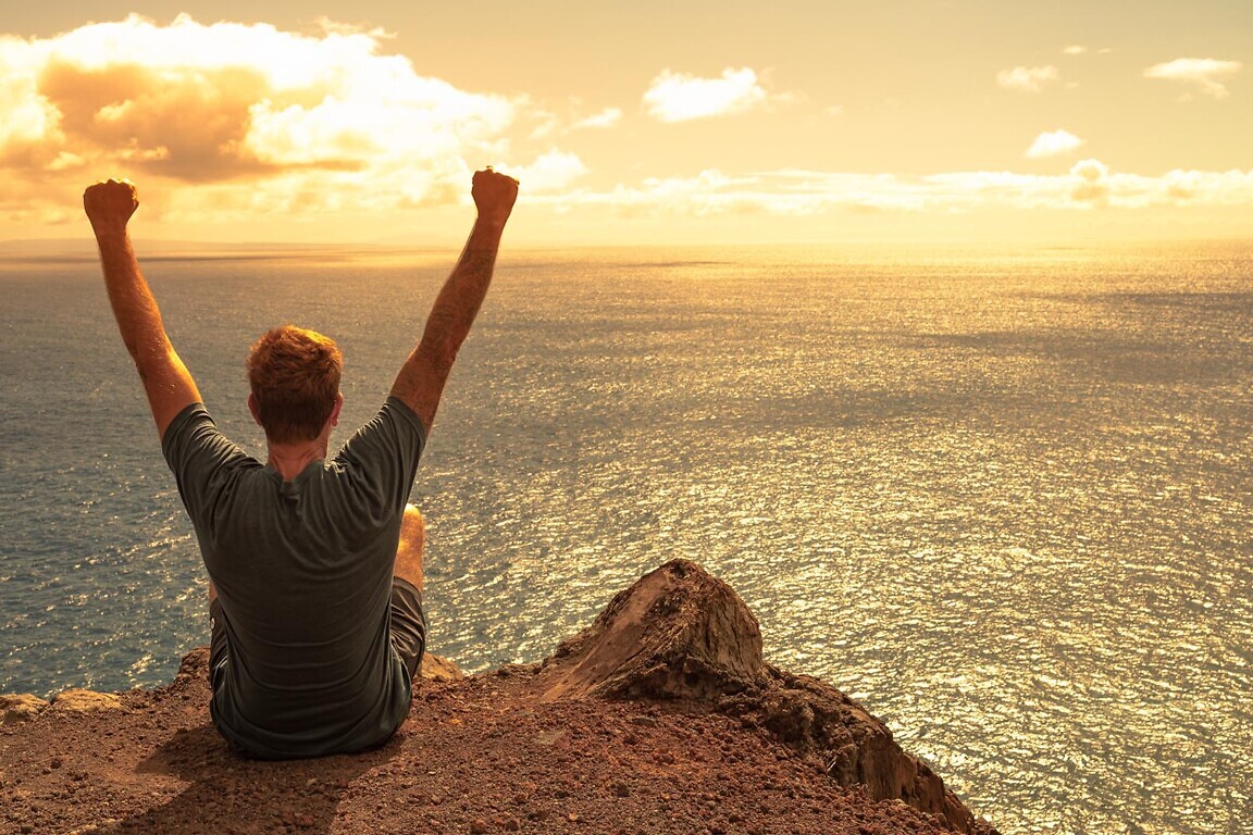 young man on edge of mountain feeling inspired hopeful looking o