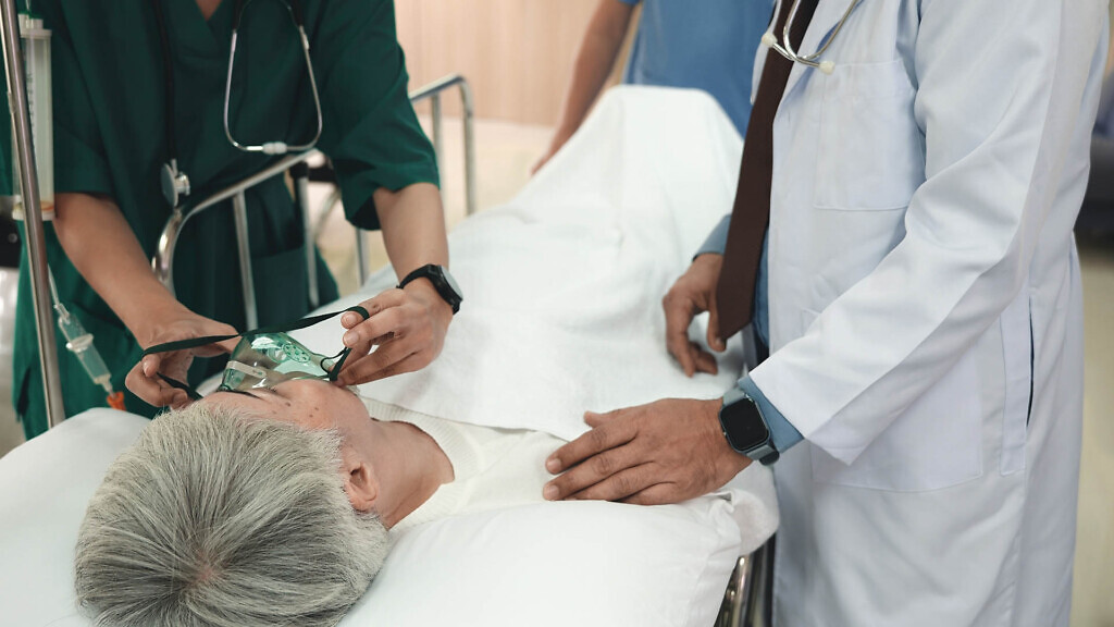 Doctor in protective equipment puts on oxygen mask to connect elderly woman patient lying in bed at hospital, anesthesiologist with mask, Patient in scrub cap with mask ventilation