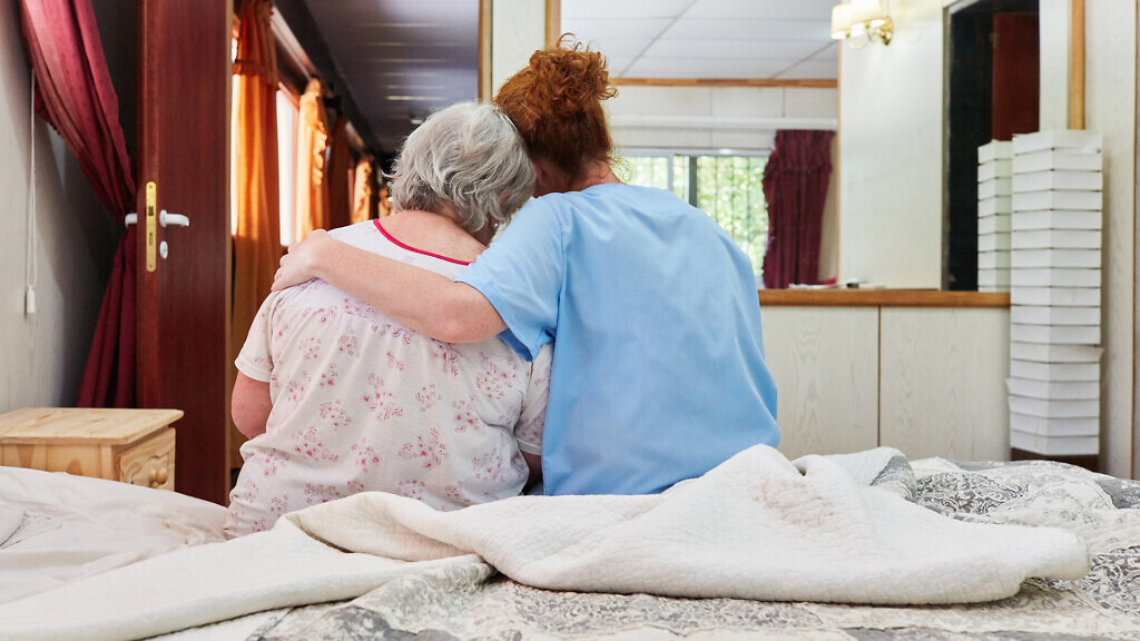 Caring geriatric nurse hugging and comforting sick senior woman in hospice or nursing home