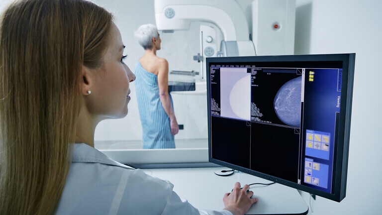 Medical technician taking mammogram exam to female patient.