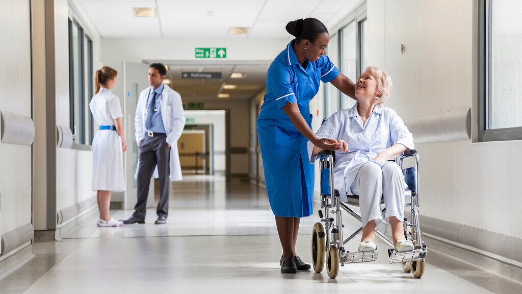 Senior female woman patient in wheelchair sitting in hospital corridor with African American female nurse and doctor