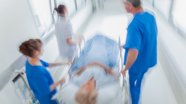 A motion blurred photograph of a senior female patient on stretcher.