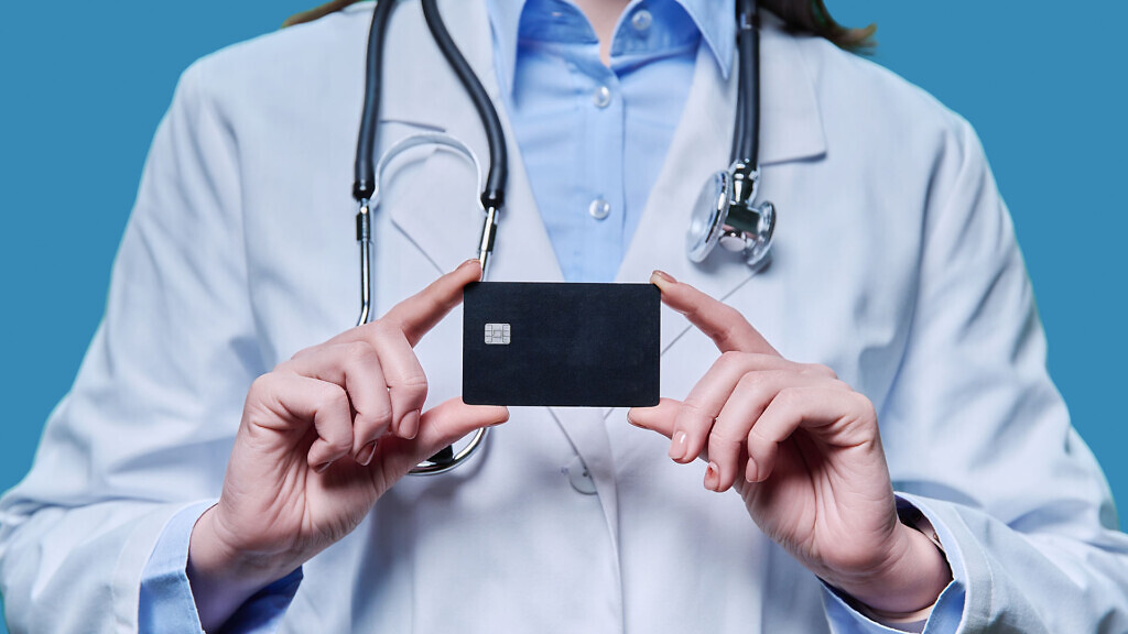 Close-up credit card in the hands of a doctor, on a blue studio background. Insurance, healthcare, medicine, credit card service concept