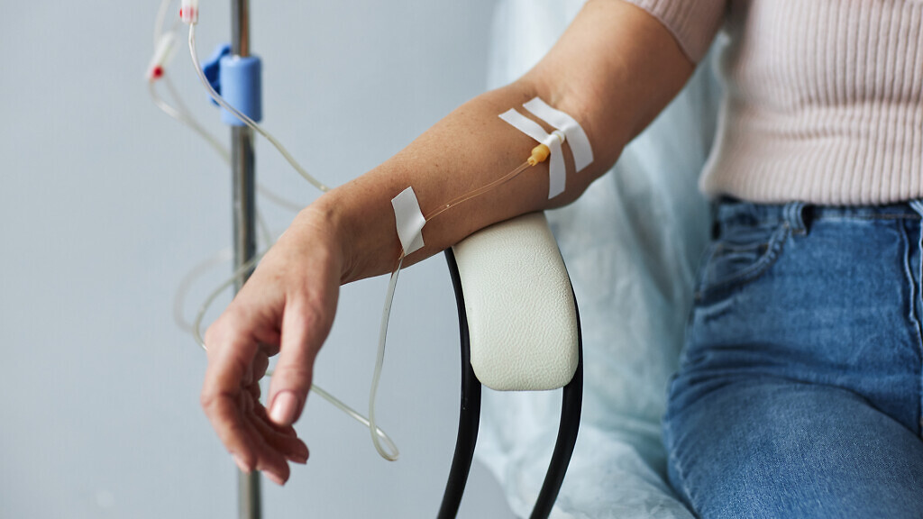 Closeup of female hand with IV drip infusion in treatment session at hospital, copy space