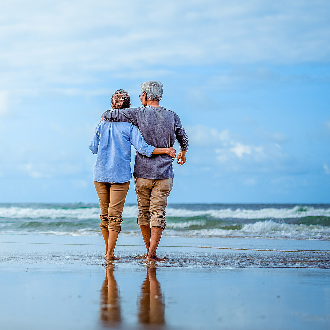 Senior couple walking on the beach holding hands at beach sunrise in evening.