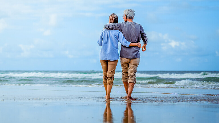 Senior couple walking on the beach holding hands at beach sunrise in evening.
