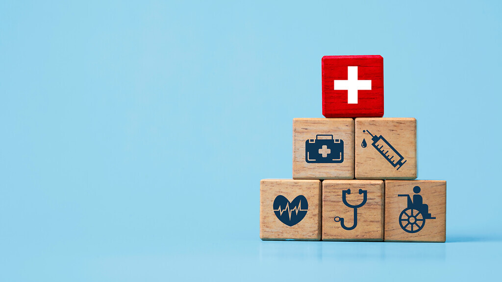 White cross on red block on top of wooden stacking with Healthcare icons.